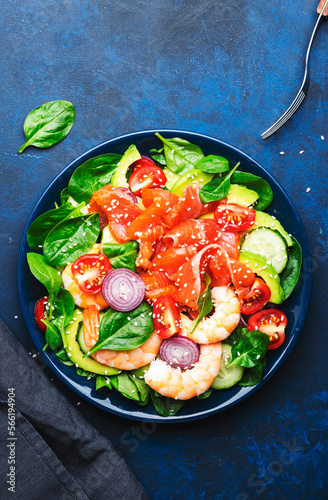 Salmon salad for ketogenic diet with shrimp, avocado, spinach, cucumber, tomato, cashew nuts, sesame. Low-carbohydrate lunch rich in healthy fats. Blue table background, top view
