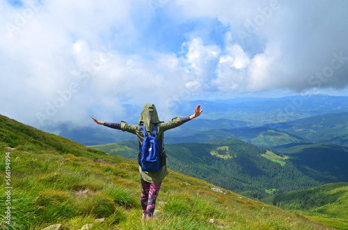 The girl is standing on a high hill. Hiking in the mountains. A girl in sportswear with a backpack. 