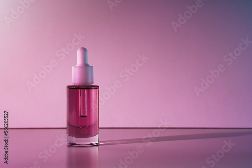 Pink face oil in glass bottle with white pipette dropper cap. Body care cosmetics background with copy space dark mood