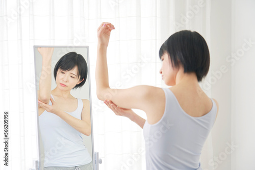 鏡の前で二の腕の贅肉を摘む女性