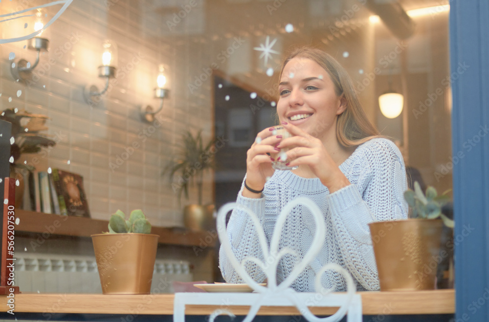 Smiling woman having coffee while sitting at table in cafe during Christmas seen through window Smiling woman having coffee while sitting at table in cafe during Christmas seen through window