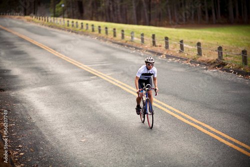 A female cyclist sprints up a hill on her bike while riding on a country road. photo