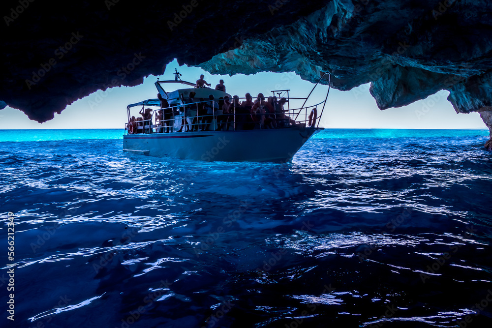 View of many tourists aboard an excursion boat being taken by the boatman to a sea cave with tropical turquoise waters in the background