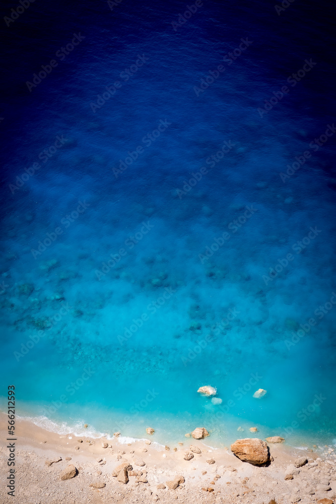 Fototapeta premium Beautiful crystal clear blue and turquoise waters next to a sandy beach with large stones in Myzithres, Zakynthos, Greece
