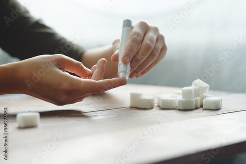 Woman hands using lancet on finger at home to check blood sugar level, glucometer and sugar cubes on wooden table close up, diabetes and health care concept