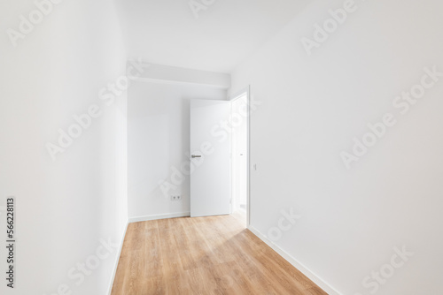 Empty narrow room with laminate flooring and newly painted white wall in refurbished apartment with corridor leading to other rooms. Repair and construction concept.