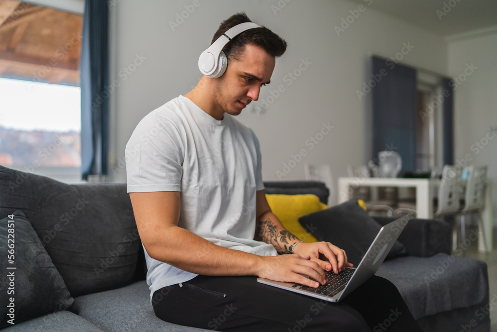 A young guy is using laptop and drinking coffee while working from home from his couch A young guy is using laptop and drinking coffee while working from home from his couch