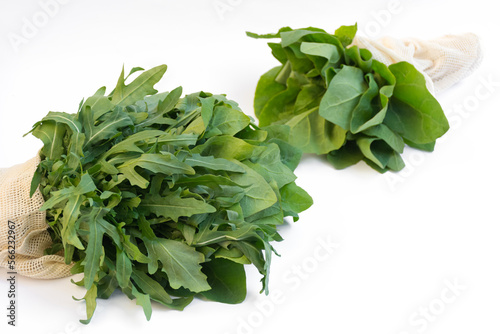 Close-up of two bunches of fresh green arugula and spinach in an eco-friendly mesh bag on white surface. View is direct. Concept of healthy eating. Ideal for dietary spring salad. Copy Space