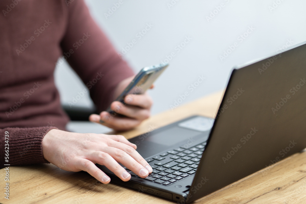Close up of a man working on laptop and using smartphone. Businessman using smartphone while working on laptop in the office on a desk Close up of a man working on laptop and using smartphone. Businessman using smartphone while working on laptop in the office on a desk
