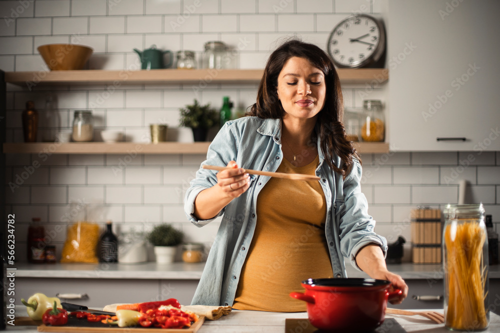 Beautiful pregnant woman preparing delicious food. Smiling woman cooking at home