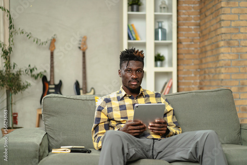 Young African man using digital tablet at home. Smiling man reading news while sitting on the couch at home. photo