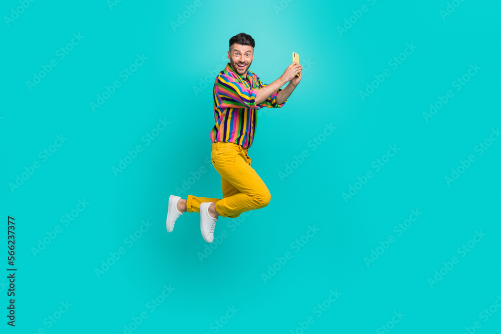 Full length size photo of funky jumping youngster guy hold smartphone take shot video call online remote conference isolated on cyan color background