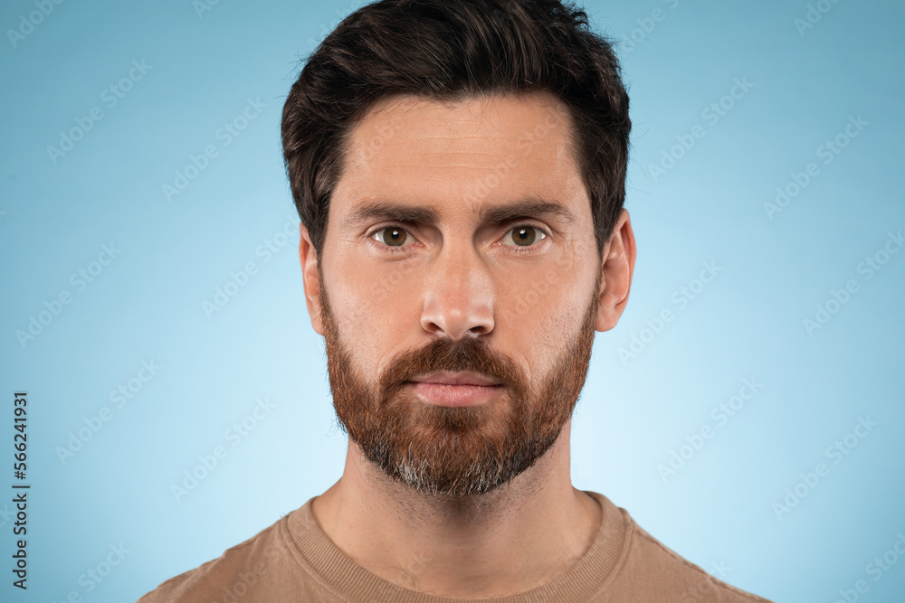 Fototapeta premium Portrait of handsome bearded man posing and looking at camera, standing over blue studio background, closeup headshot