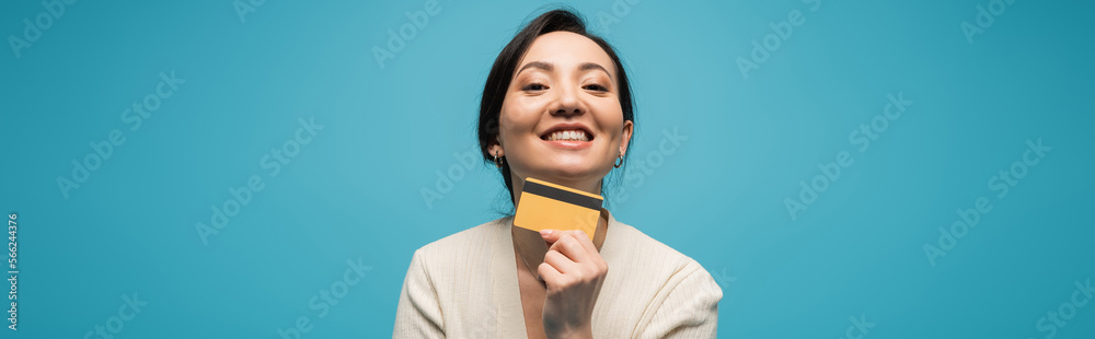 Smiling asian model holding credit card isolated on blue, banner Smiling asian model holding credit card isolated on blue, banner