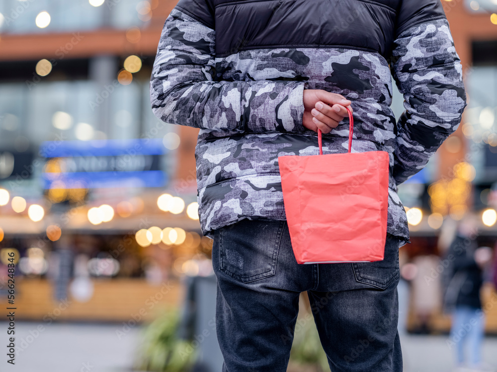 Man holding bag with Christmas present behind back Man holding bag with Christmas present behind back