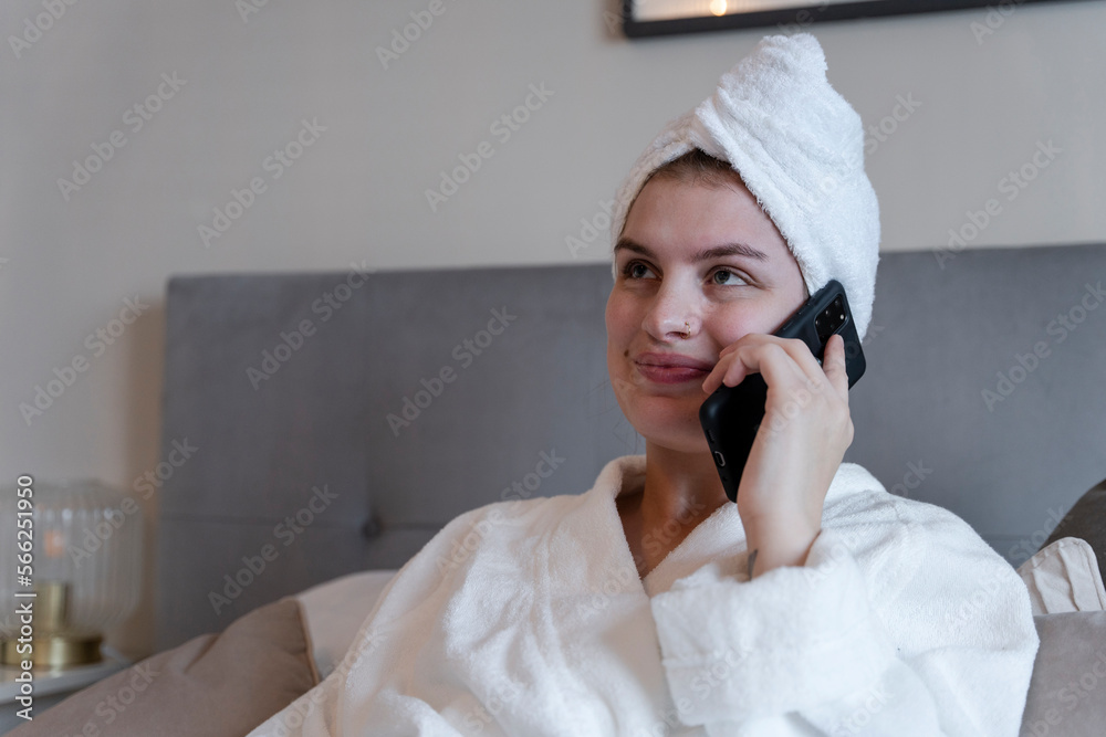 Woman in bathrobe and towel turban talking on smart phone on bed Woman in bathrobe and towel turban talking on smart phone on bed