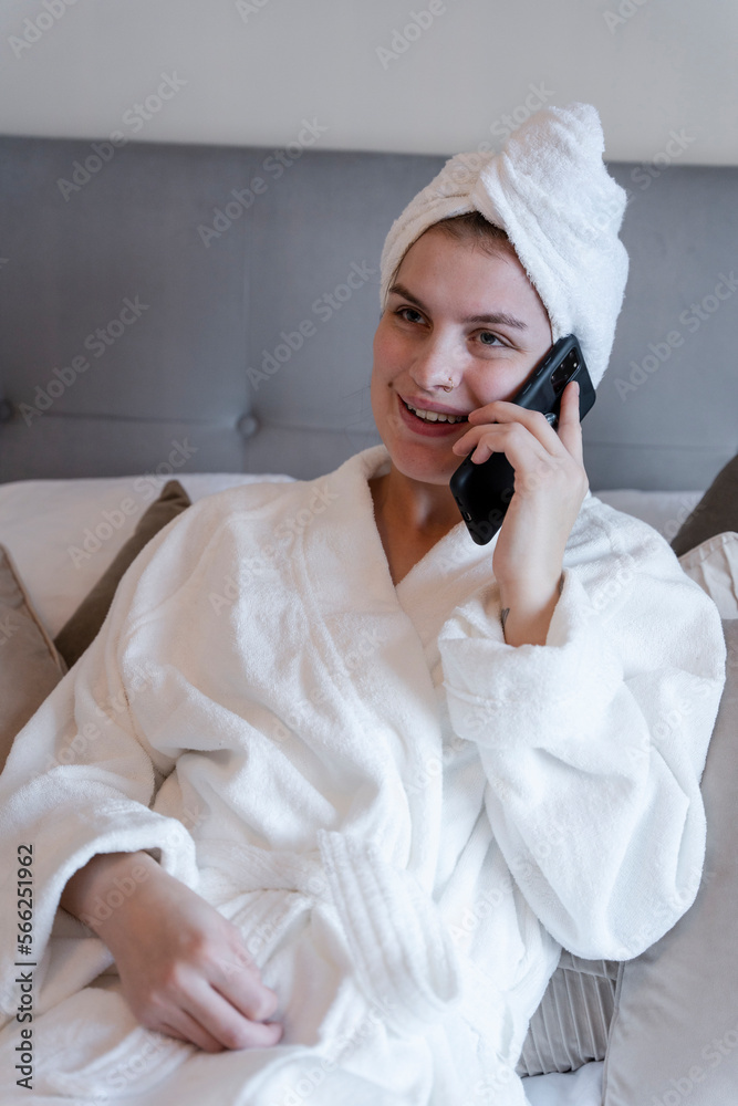 Woman in bathrobe and towel turban talking on smart phone on bed Woman in bathrobe and towel turban talking on smart phone on bed