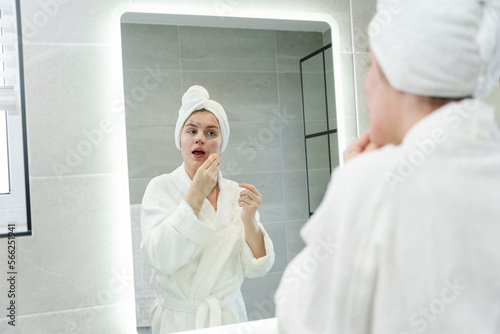 Woman in bathrobe cleaning face in front of bathroom mirror photo