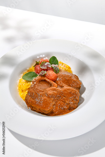 Traditional italian dish - osso buco with risotto milanese. Stew meat on bone with rice on white plate. Summer italian dining. Italian osso buco with garnish with hard shadows