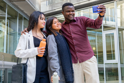 Happy attractive coworkers taking a selfie with a smartphone outside the office. Group of young friends smiling in a work break in the city. Ethnic diversity and social inclusion. Copy space. © Clàudia Ayuso