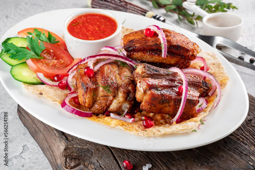 Pieces of pork kebab on a plate with pita bread and fresh vegetables. Grilled Pork Dishes, close up