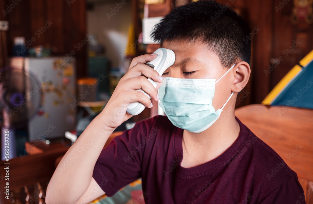 Asian kids boy wearing a mask looks uncomfortable use temperature taken for the scan of fever with an infrared thermometer on his own at home