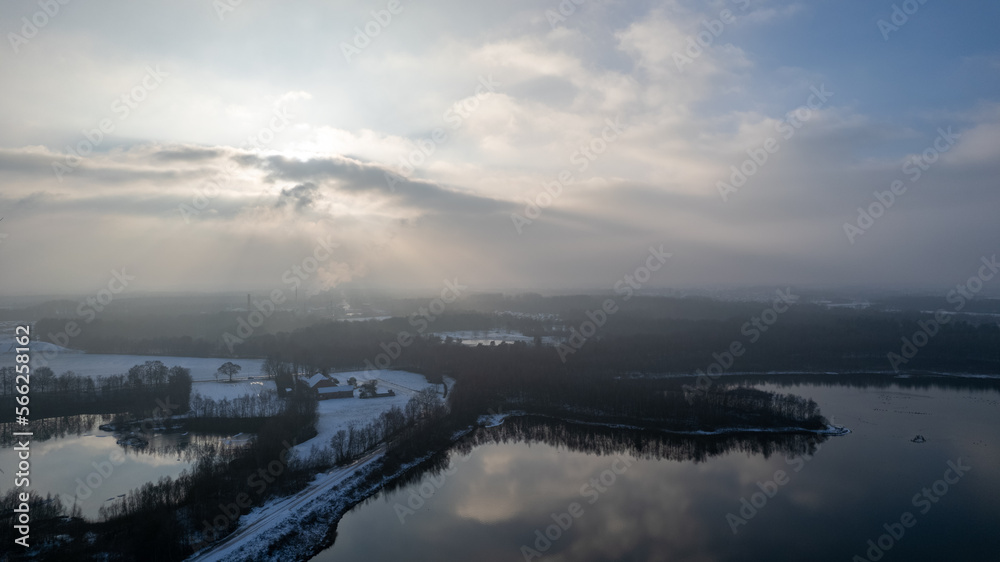 Obraz premium Aerial landscape of the frozen lake and forest in the snow in Belgium at sunset shot by a drone. High quality photo
