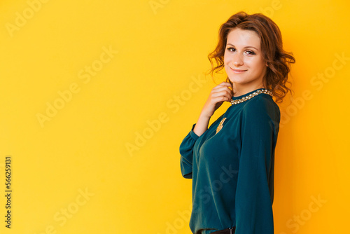 A beautiful brunette girl in a green blouse with a golden brooch in the form of the moon poses against a yellow background. The girl looks at the camera and smiles