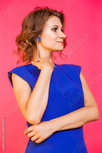 Beautiful long earrings on a young woman in a blue dress. Girl posing on a red fuchsia background