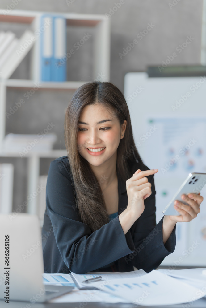 Beautiful Asian female bookkeeper doing online accounting with laptop in private accounting office, balance sheet and stock market statistics.