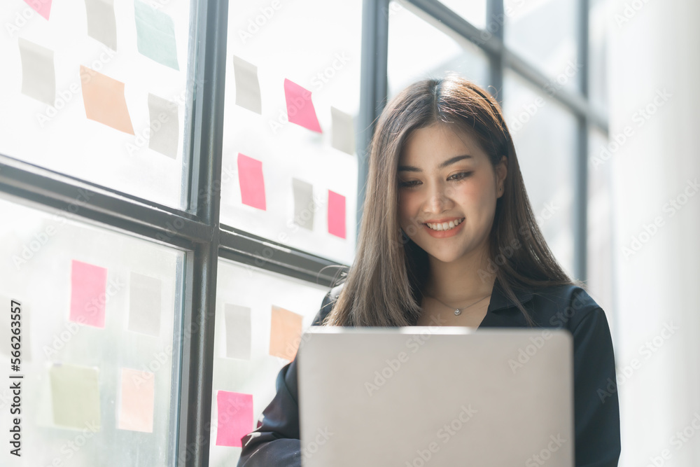 Using laptop, Pretty asia business woman bookkeeper brainstorming and working in modern office workplace with sticky notes or post it at windows.