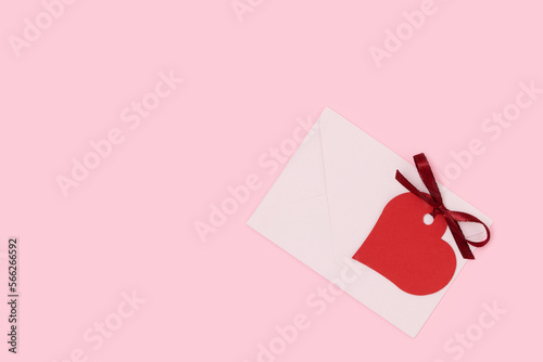 Red empty tag in a heart shape with tied ribbon bow and envelope on a pink background. Holidays concept.