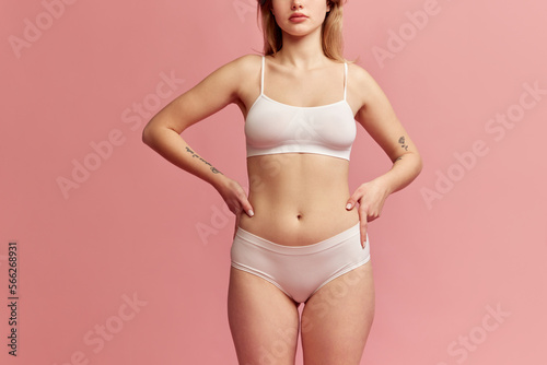 Studio shot of young slim woman wearing white inner wear posing over pink color background. Concept of natural beauty, body and skin care, healthy eating