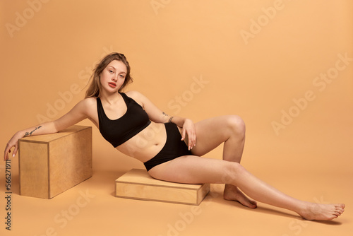 Portrait of young slim beautiful girl wearing black underwear posing over sand color background. Concept of beauty, body and skin care, healthy eating