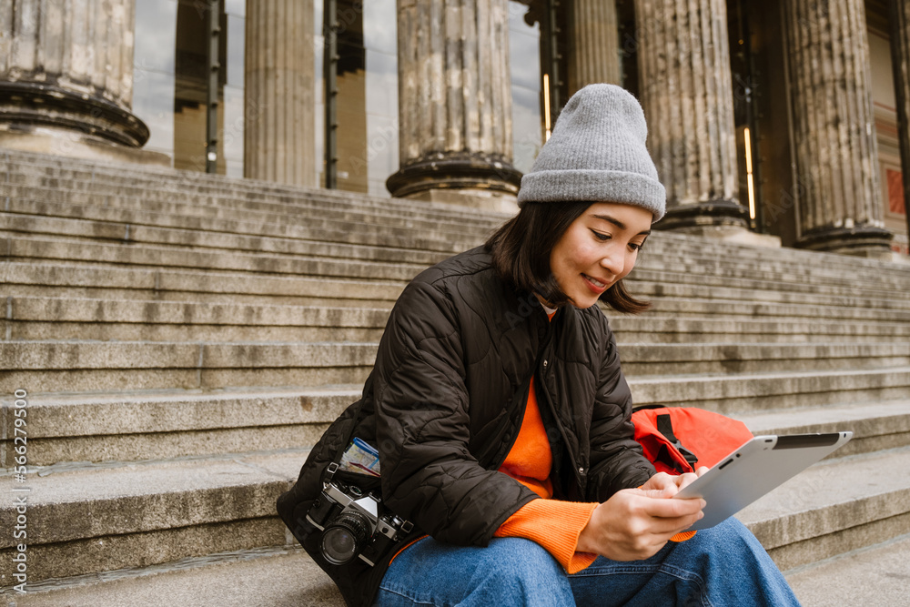 Smiling asian girl tourist using digital tablet while sitting on stairs