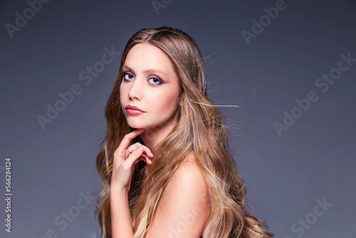 Beautiful woman with long and shiny wavy hair and makeup. Model girl with curly hairstyle looking at camera