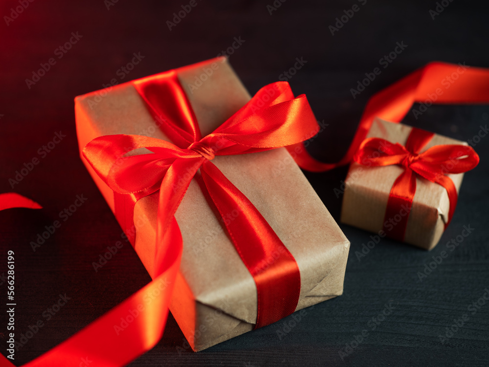 Two gift boxes packed in kraft paper with a red ribbon on a dark table Two gift boxes packed in kraft paper with a red ribbon on a dark table
