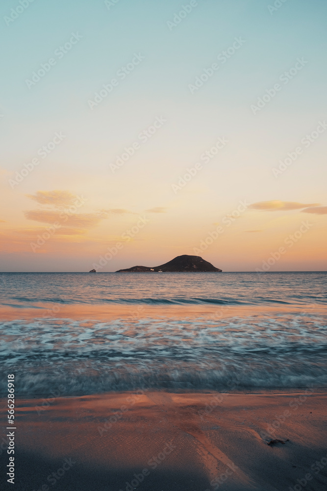 Vertical ocean sunrise landscape with island and colorful sky in background. Waves and shores on sea water in morning light. Empty sky copyspace. Beauty nature seascape in sunset moody evening dusk.