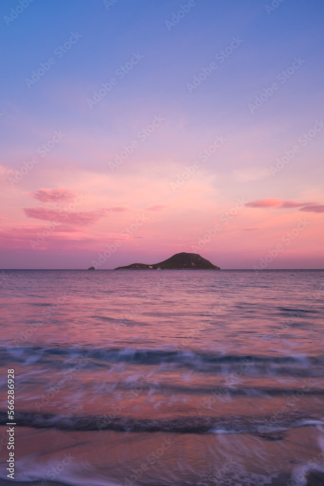 Pink color sunset on the ocean with island in background. Concept of travel and scenic place destination. Long exposure on ocean waves. Empty sky on horizon to write your text. Copy space.