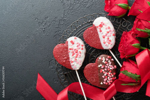 Rose red flowers, brownie cookies and chocolate candy on heart shaped, gift box with wine on black background. Valentines day, Mothers or Womens Day greeting card. Top view flat lay with copy space.