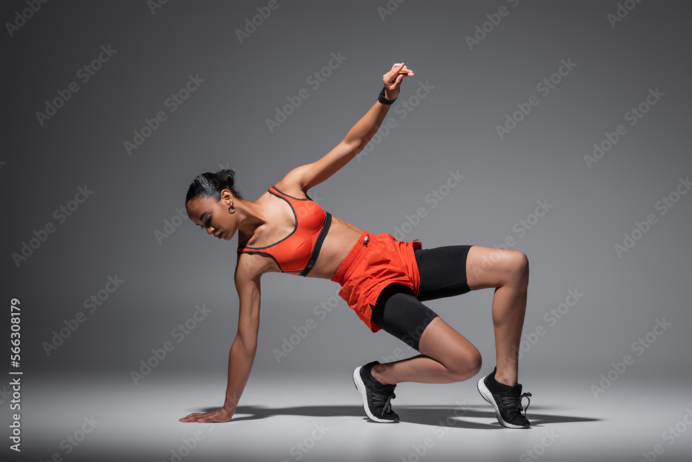 full length of strong and sportive african american woman working out on grey background.