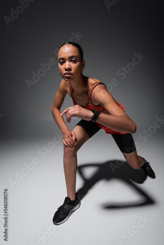 full length of brunette african american woman in sportive shorts exercising on grey.
