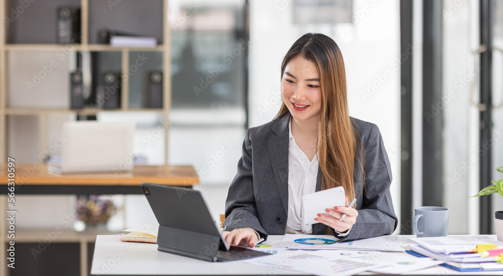 Young business Asian woman is sitting at table, working on laptop with graphs, charts, money and report financial concepts. Online marketing, education, analytics, e-commerce, business planning