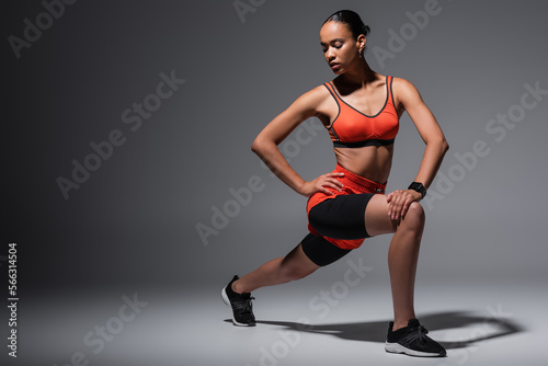 full length of young african american woman in sportswear and sneakers exercising with hand on hip on grey.