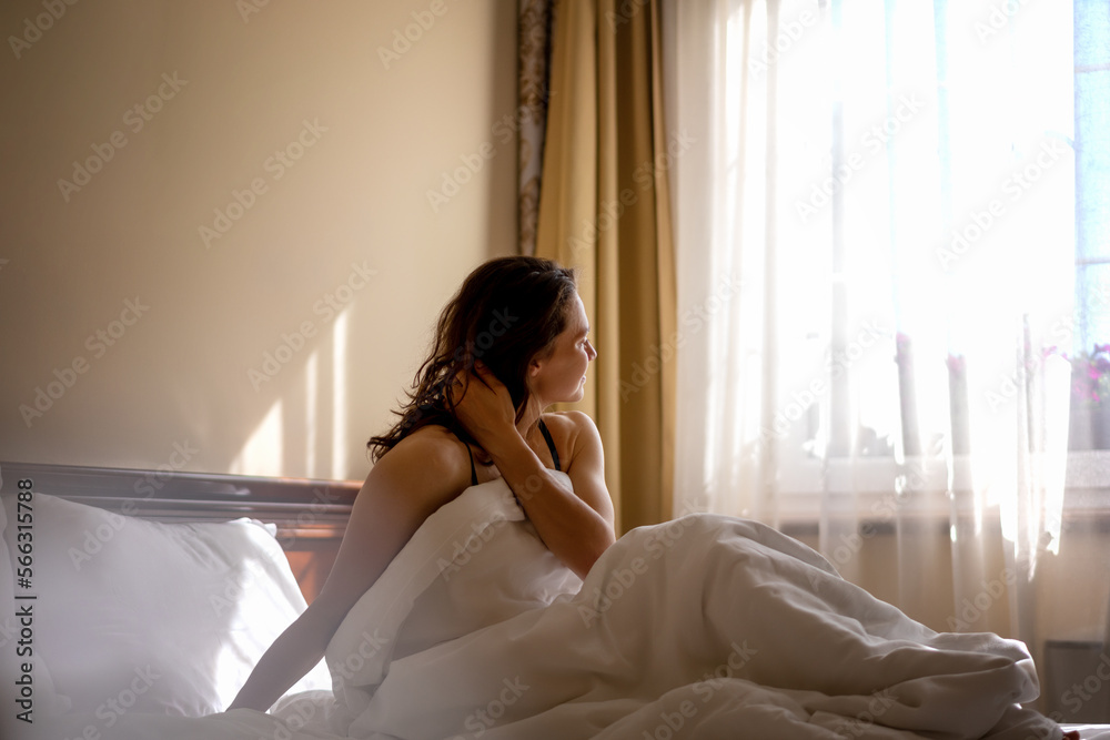 Beautiful young happy relaxed woman in the morning sitting in bed under blanket