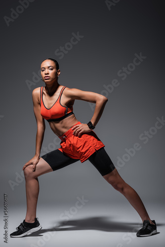 full length of young african american woman in sportswear and sneakers exercising with hand on hip on grey.