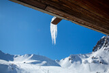 Cold winter weather in the mountains with snow in the Alps. Mountain landscape with ice stalactites hanging from a roof.
