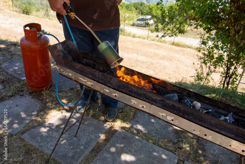 A man with a gas blowtorch ignites charcoal in a barbeque. A man lights coal with a blow torch. Man with a butane gas tank. photo