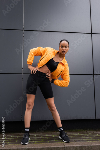 full length of brunette african american sportswoman in bike shorts and yellow puffer jacket exercising with hands on hips. © LIGHTFIELD STUDIOS