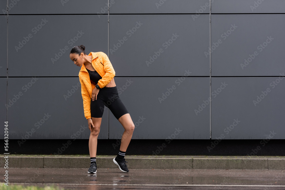 full length of african american sportswoman in stylish sneakers and yellow puffer jacket posing outside. full length of african american sportswoman in stylish sneakers and yellow puffer jacket posing outside.